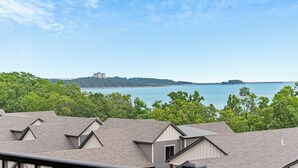 A residential area with multiple houses, a clear view of a large body of water, and a distant island with buildings. - 2 bed lake condo, Resort Amenities, Ticket & Golf Discounts, just 2 minutes to Silver Dollar City (Branson)