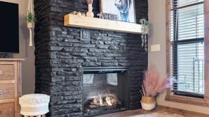 A stone fireplace with a fire, a wooden shelf above it, and a window with blinds. - 2 bed lake condo, Resort Amenities, Ticket & Golf Discounts, just 2 minutes to Silver Dollar City (Branson)