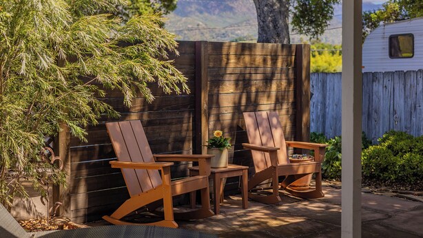 A wooden deck with two rocking chairs and a small table, surrounded by a wooden fence and a tree.