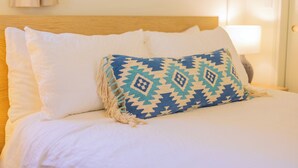 A neatly made bed with white linens and a single decorative pillow with a geometric pattern.