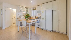 A modern kitchen with white cabinets, a wooden countertop, a gas stove, a refrigerator, and a dining area with a table and chairs.