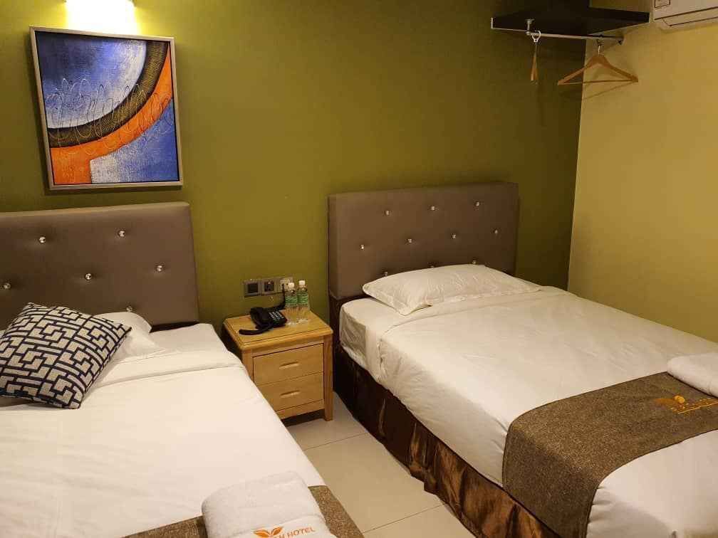 Habitación de hotel con dos camas, una mesita de noche con teléfono y artículos de aseo, y un cuadro en la pared.