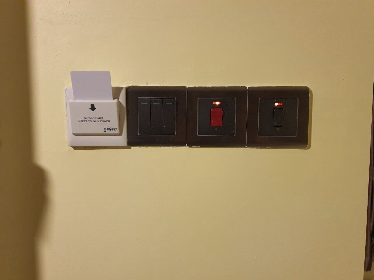A wall-mounted electrical panel with a card slot labeled "Mifare Card Insert to Gain Power" and three switches.