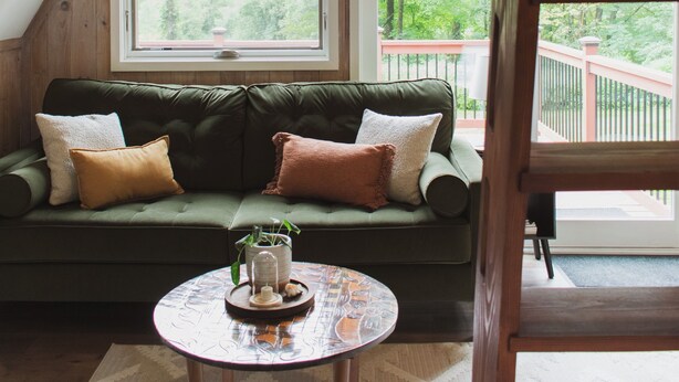 A cozy room with a green sofa, a round coffee table, and a large window offering a view of the outdoors.