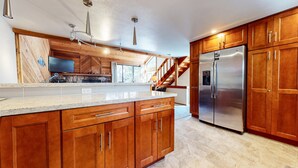 A kitchen with wooden cabinets, a stainless steel refrigerator, and a granite countertop. - Mammoth Sierra Townhomes #38 3 Bedroom Condo (Mammoth Lakes)