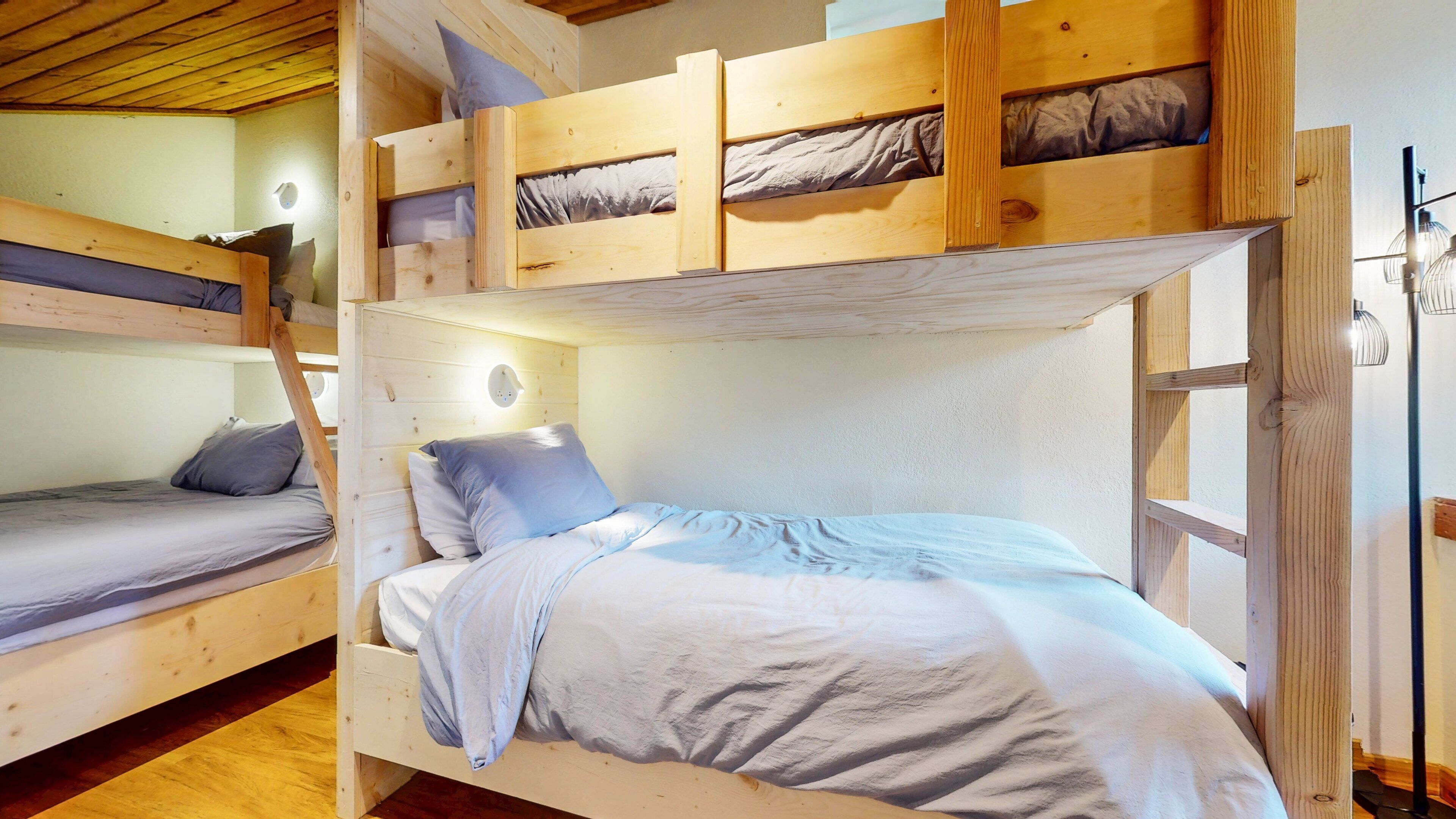 Dormitorio con literas, techo de madera, ventana y lámpara fijada a la pared.