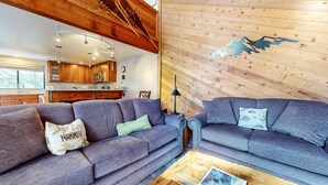 A cozy living room with two grey sofas, a coffee table, and a wooden wall with a mountain design. - Mammoth Sierra Townhomes #38 3 Bedroom Condo (Mammoth Lakes)