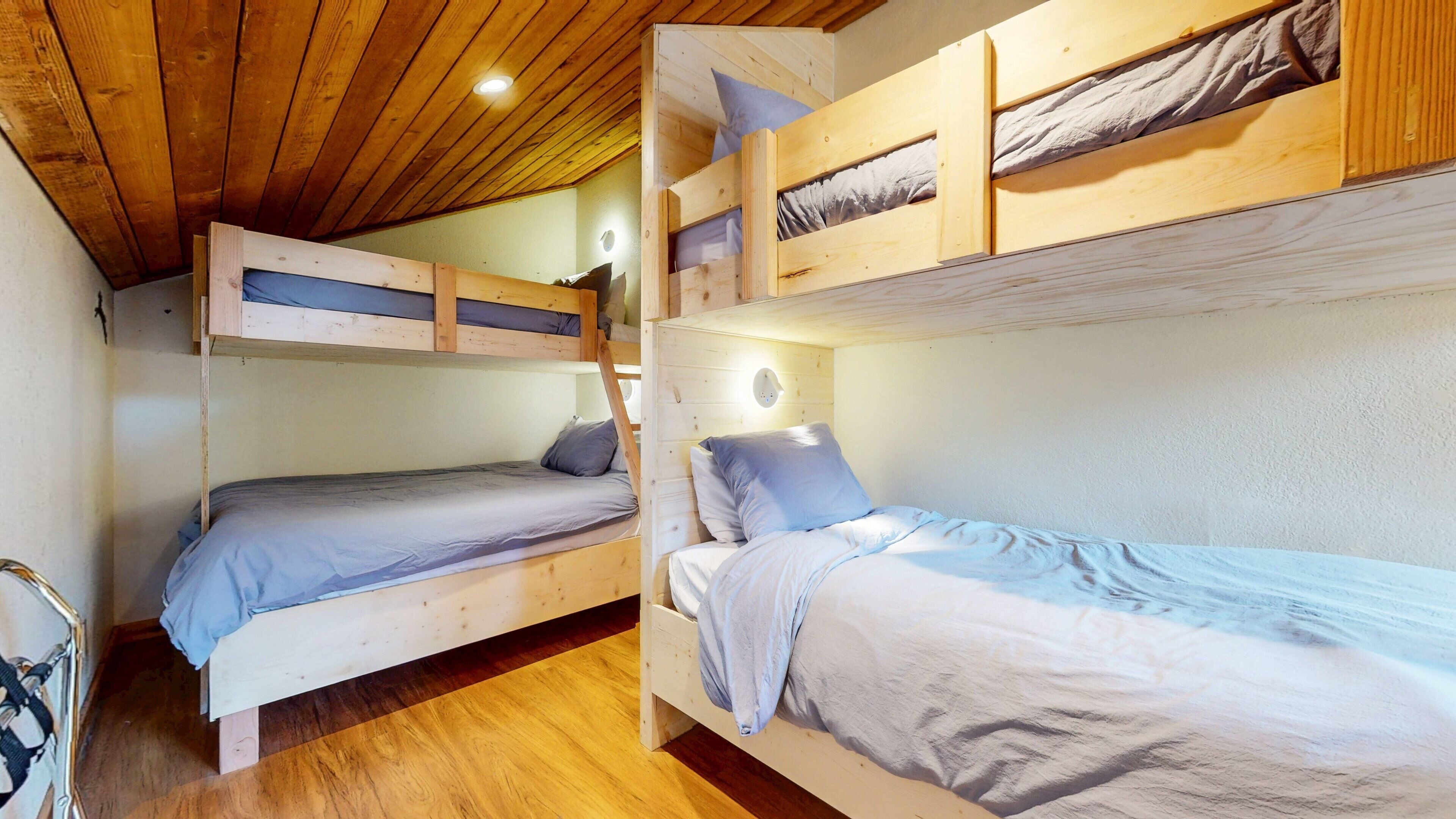 Una habitación con tres literas, suelo de madera y una lámpara en el techo.
