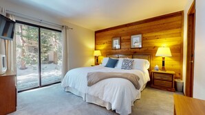 A bedroom with a large bed, two bedside lamps, a wooden headboard, and a sliding glass door leading to a snowy outdoor area. - Mammoth Sierra Townhomes #38 3 Bedroom Condo (Mammoth Lakes)
