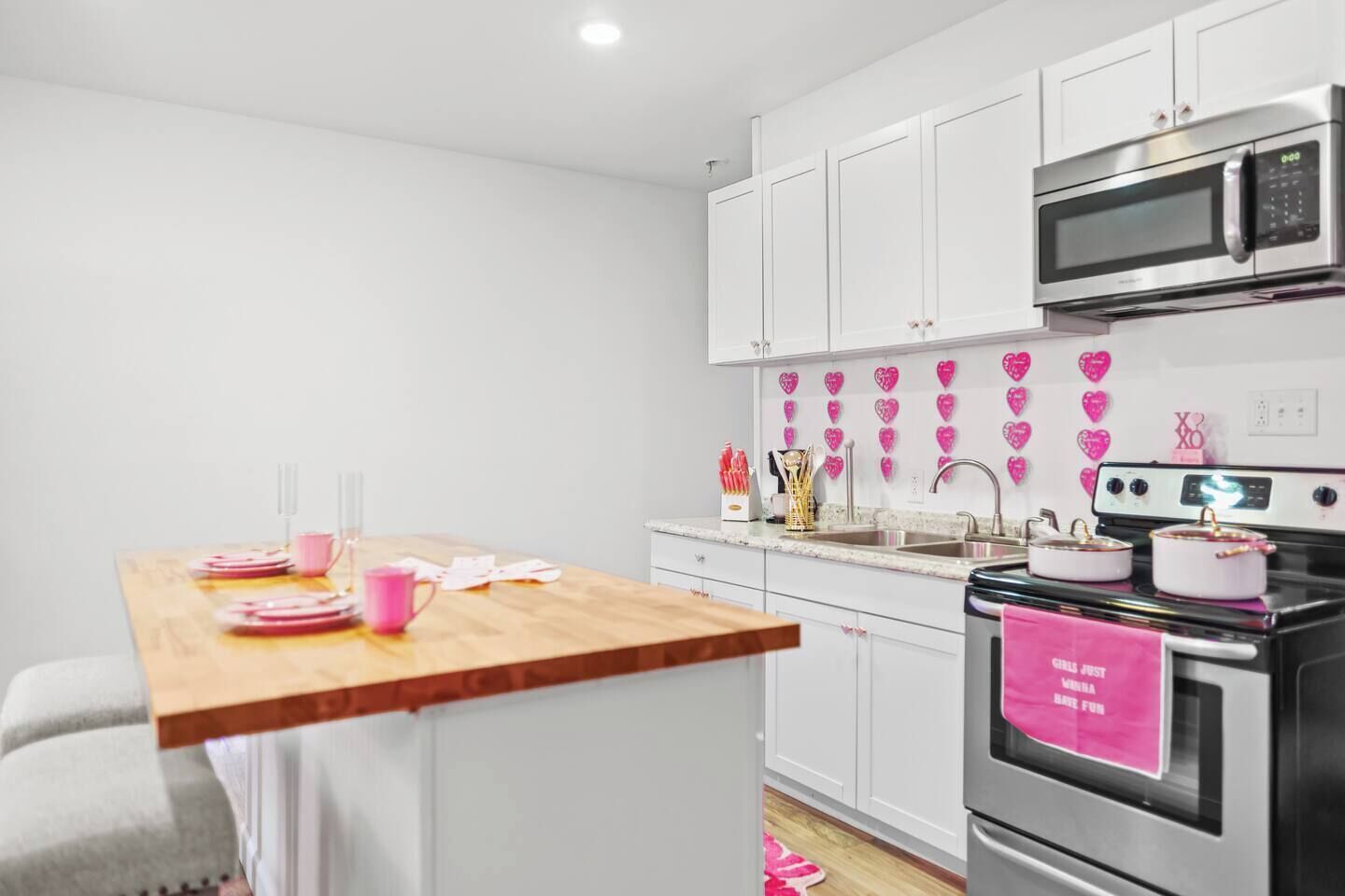 Eine moderne Küche mit weißen Schränken, einem Holztisch und Wanddekorationen in Herzform, pink.