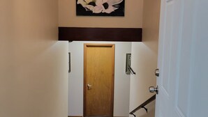 A hallway with a wooden door at the end, a light fixture above, and a framed floral artwork on the wall.