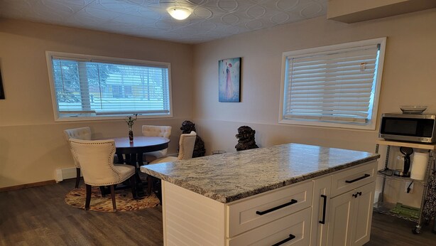 A kitchen with a granite countertop, white cabinetry, and a dining area with a round table and chairs.