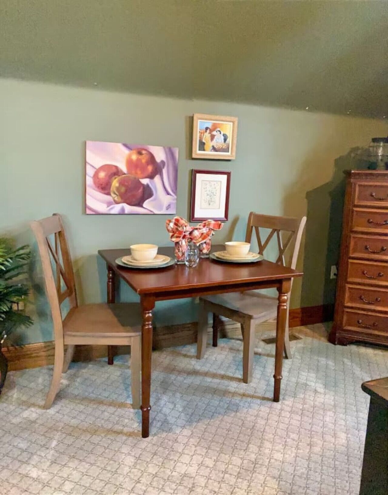 Un comedor con una mesa y sillas de madera, un jarrón con arreglo floral, y dos cuadros en la pared.