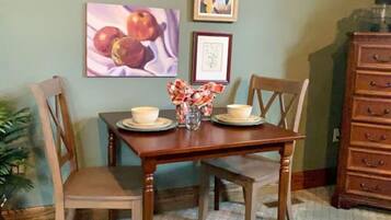 Un comedor con una mesa y sillas de madera, un jarrón con arreglo floral, y dos cuadros en la pared.