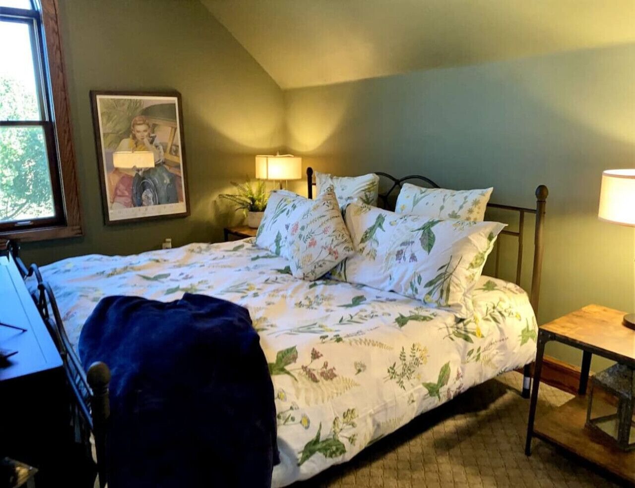 Quarto com cama, mesas de cabeceira, janela e um quadro na parede.
