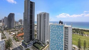 Un immeuble de grande hauteur à la façade incurvée, situé à côté d’un bâtiment moderne à la façade ornée, surplombant une zone côtière sous un ciel dégagé.