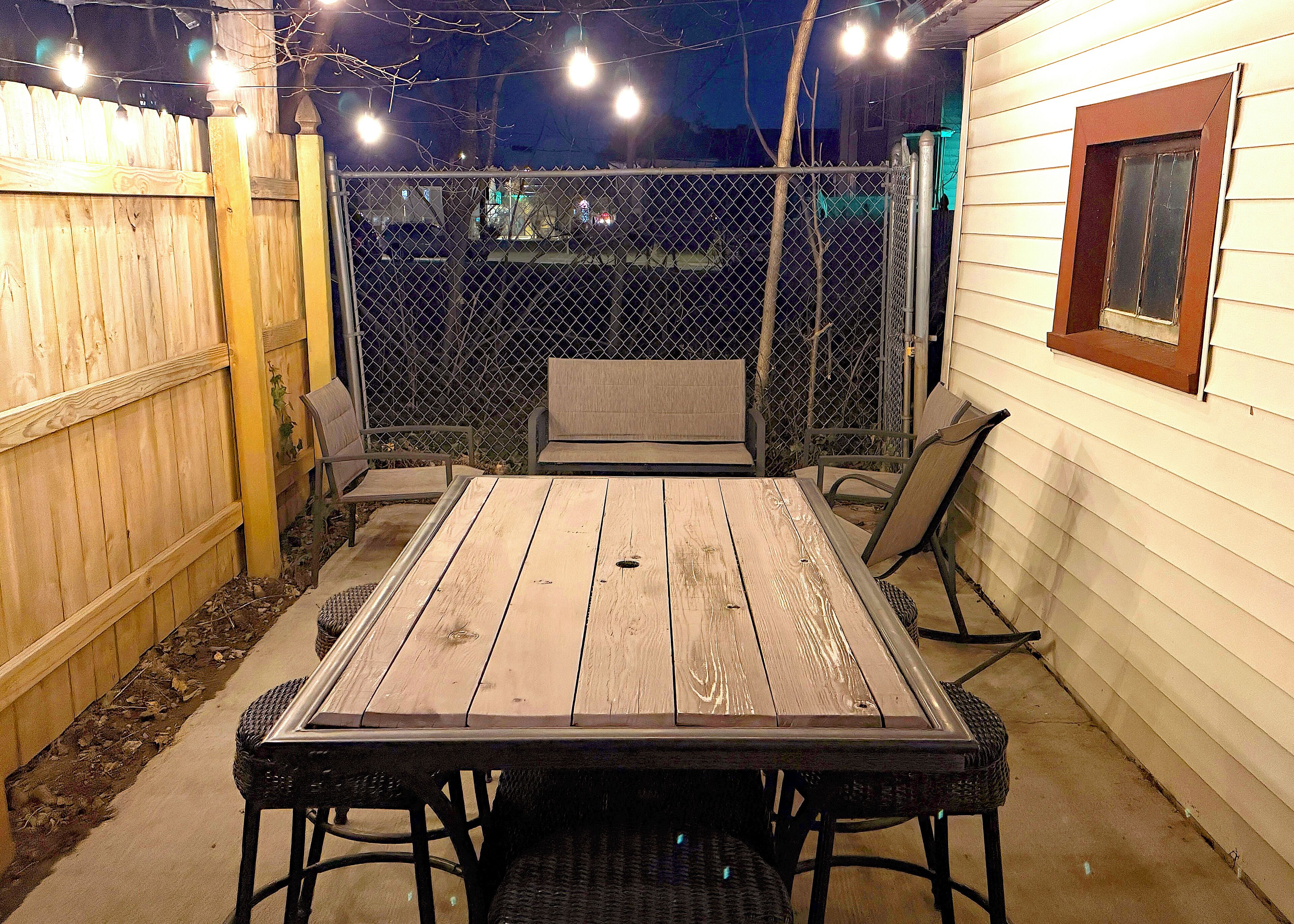A patio with a wooden table and chairs, a wooden fence, and a window with a brown frame.