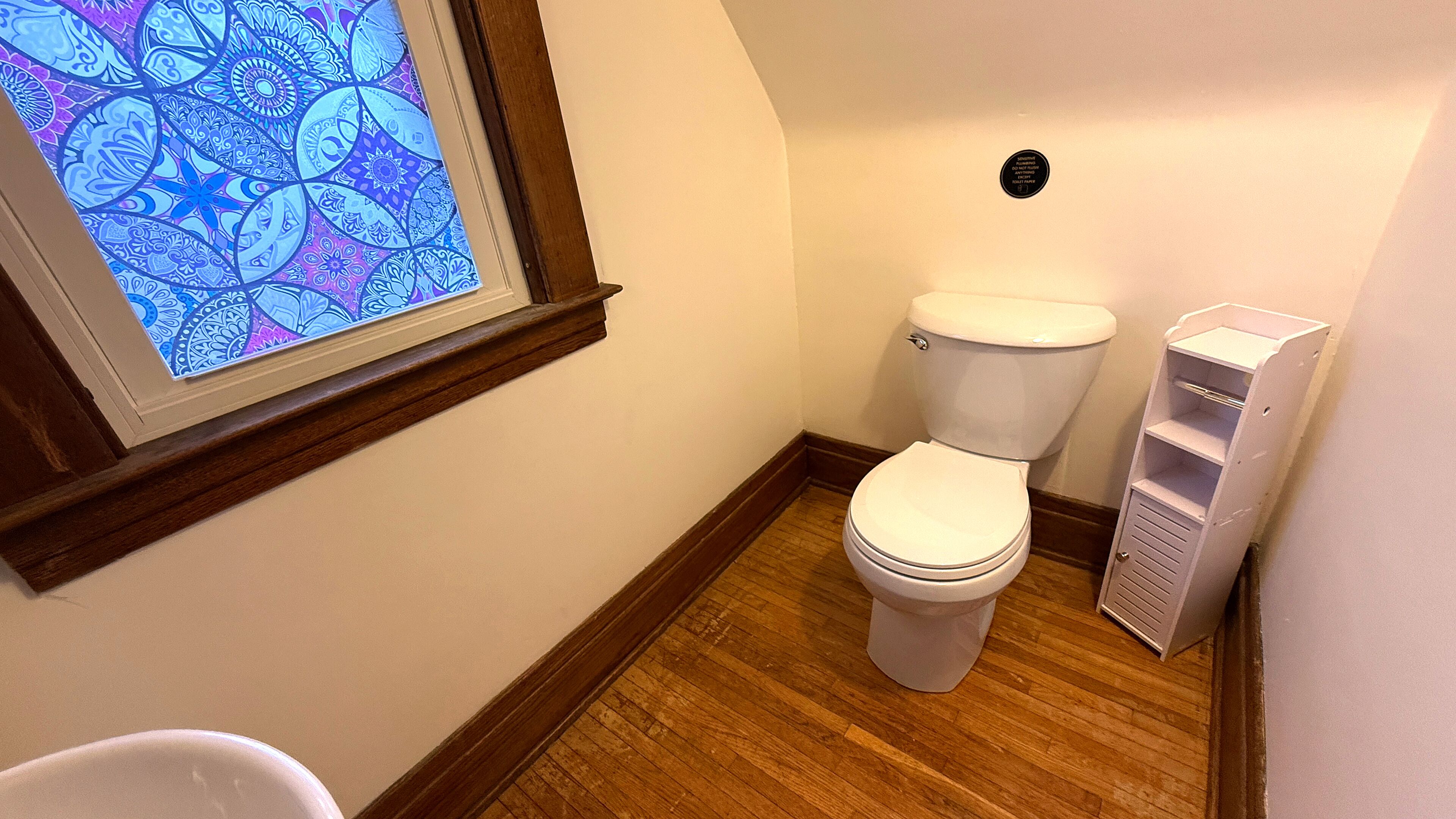 Un baño pequeño con inodoro, suelo de madera y una ventana con diseño de vitral.