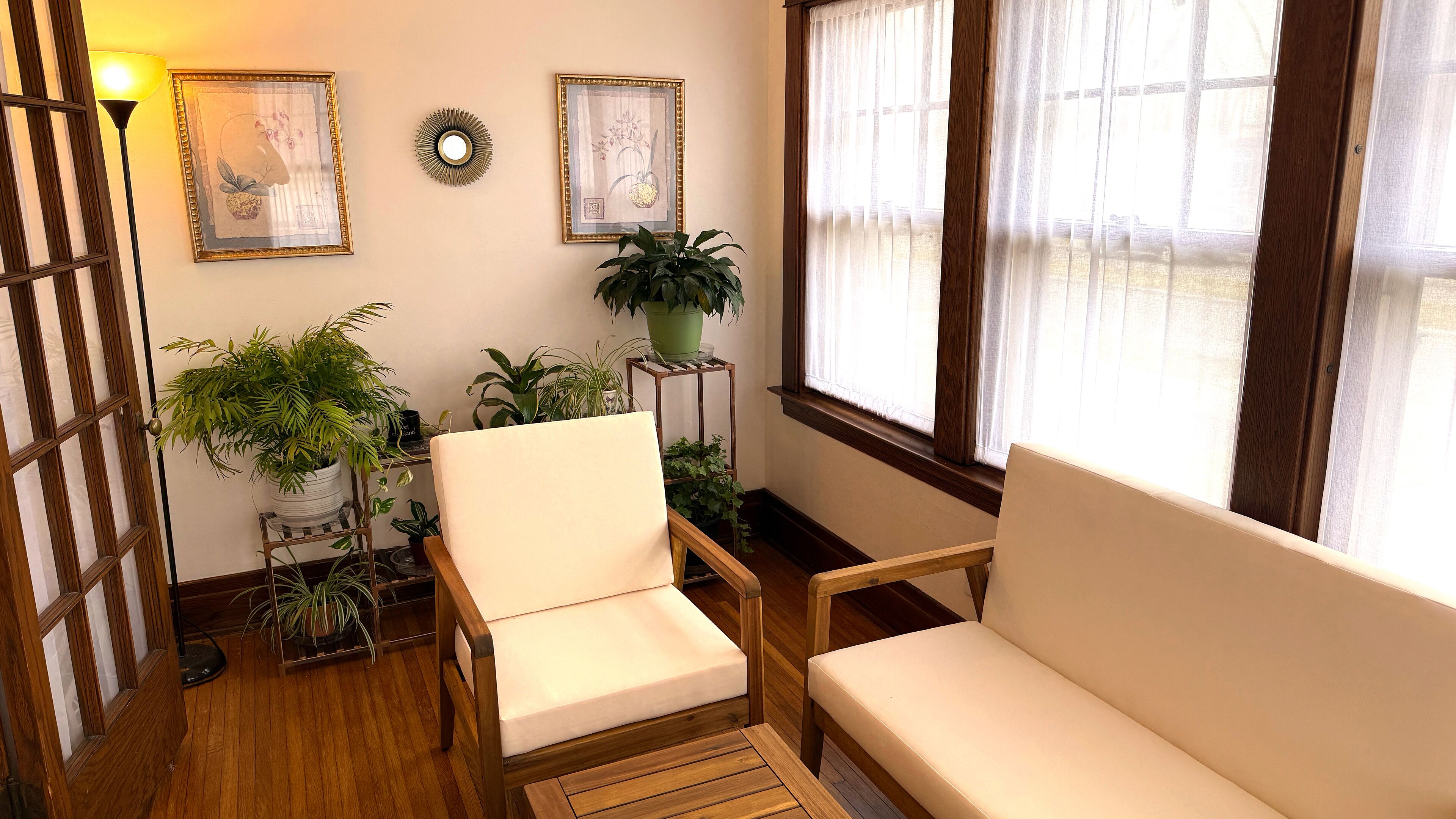 A cozy room with two white armchairs, wooden flooring, a potted plant, and framed artwork on the wall.