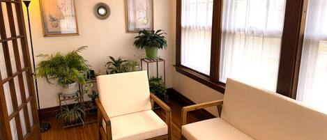 A cozy room with two white armchairs, wooden flooring, a potted plant, and framed artwork on the wall.