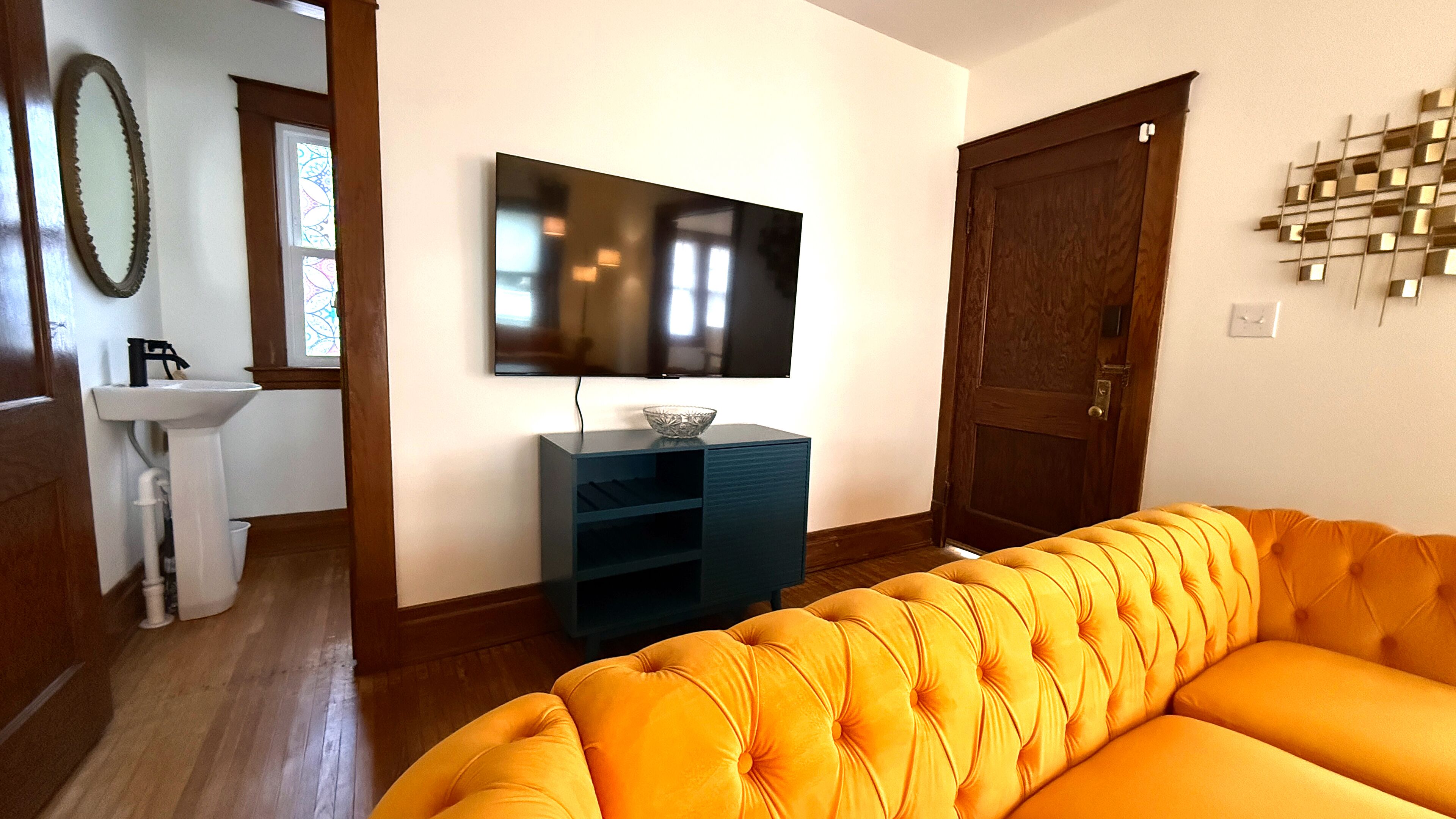 Ein Wohnzimmer mit einem großen Flachbildfernseher an der Wand, einer blauen Unterhaltungsanlage, einer Holztür und einem leuchtend orangefarbenen Sofa.