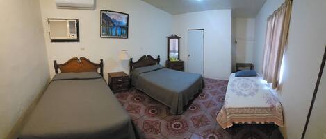 A room with two beds, a nightstand, a dresser, an air conditioner, a painting, and a door.