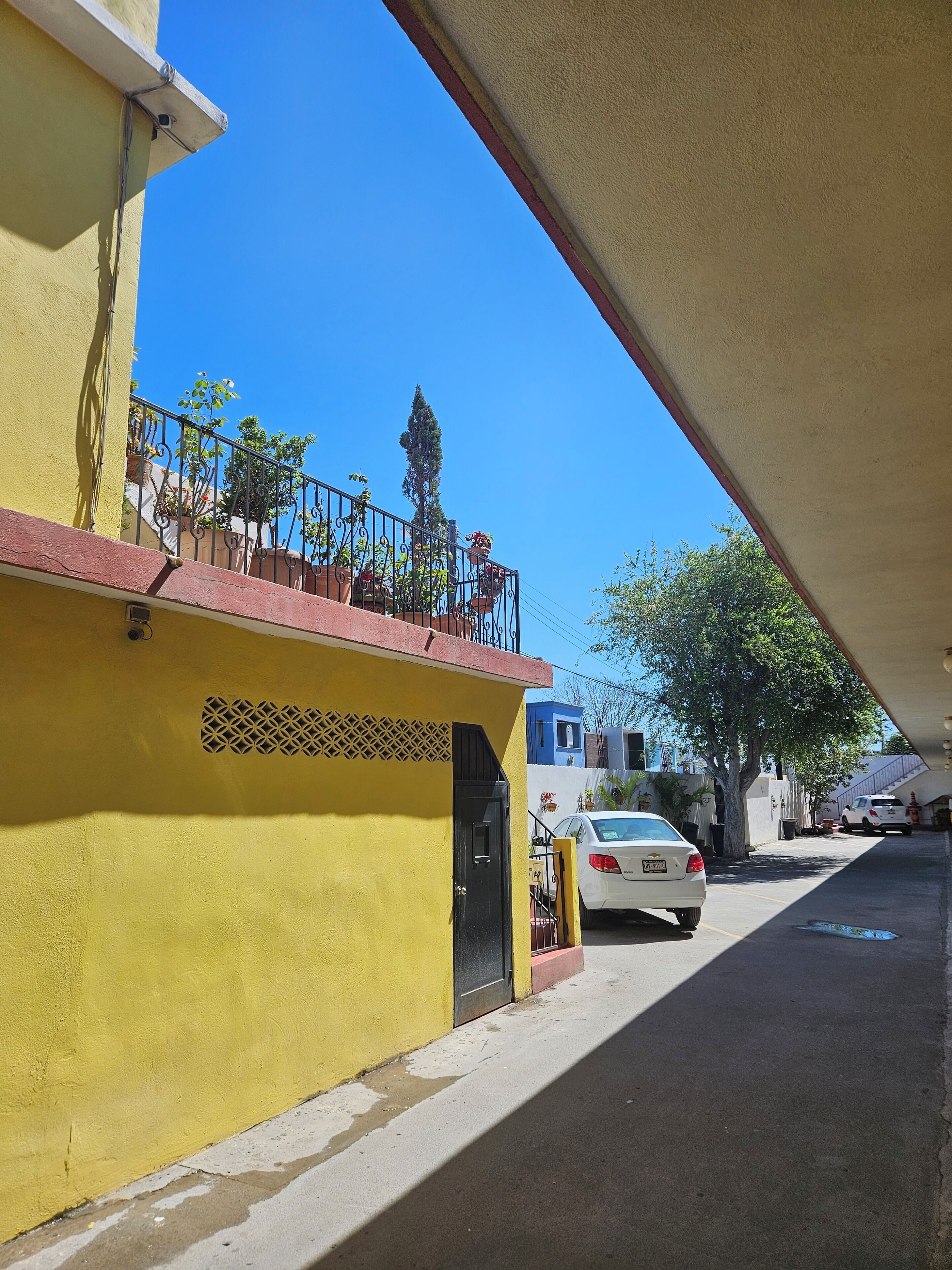 Un edificio amarillo con un balcón, una puerta negra y un coche blanco estacionado en la calle.