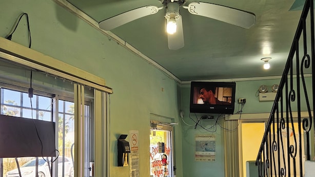 A hallway with a ceiling fan, a television mounted on the wall, a staircase with a metal railing, and a door with a window. - Hotel Chalet (Matamoros)