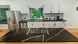 A modern kitchen with a central island, white cabinets, and a view of greenery through a window. - Spacious & Game room in Irving 15 min to Airport& downtown Dallas (Irving)