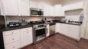 A modern kitchen with white cabinets, stainless steel appliances, and a herringbone tile backsplash.
