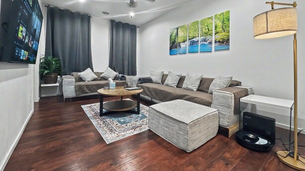 A modern living room with a sofa, a coffee table, a rug, a ceiling fan, and a painting on the wall.