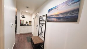 A hallway with a bench, a painting of a sunset over the ocean, and a door with a decorative metal gate.