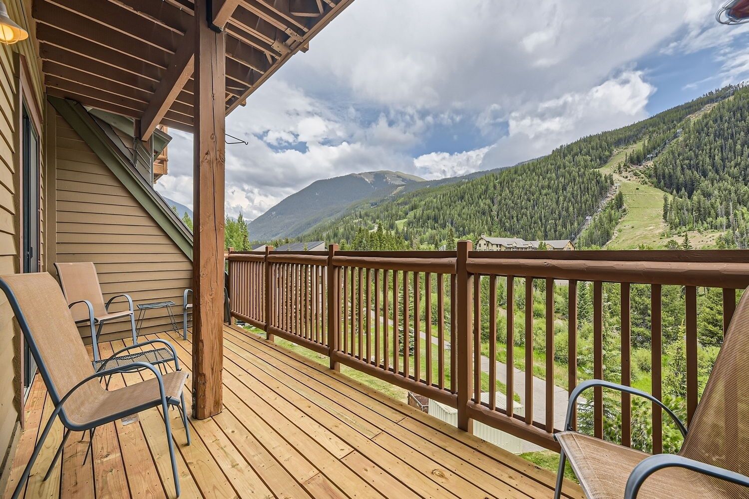A wooden deck with chairs and a railing overlooking a mountainous landscape.