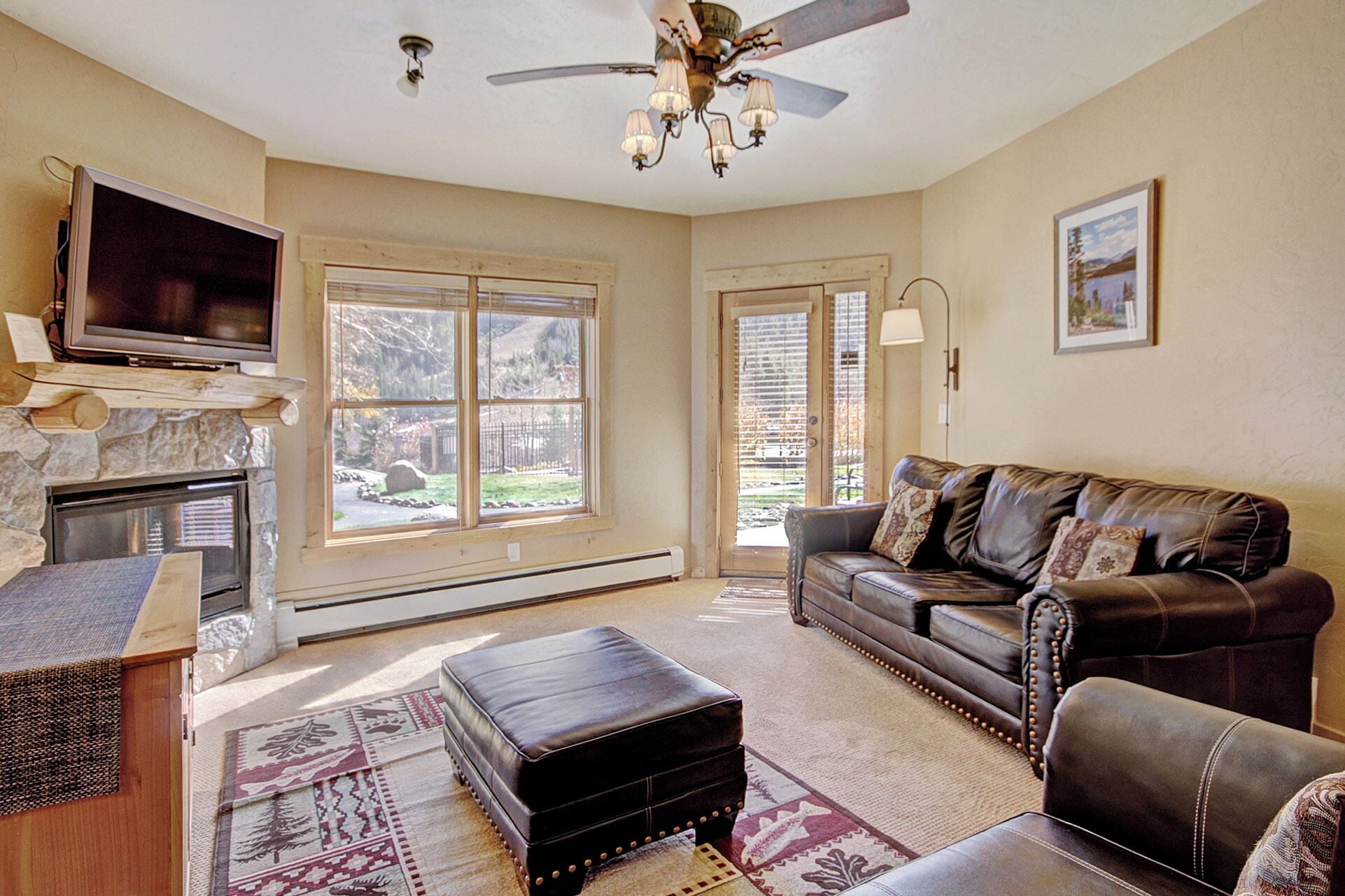 A living room with a stone fireplace, leather sofa, and a flat-screen TV mounted above it.
