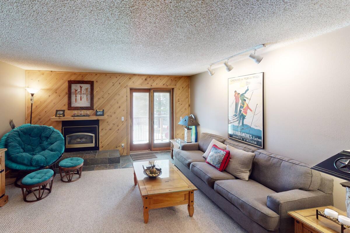 Una sala de estar acogedora con chimenea, un sillón azul verdoso, un sofá y un televisor de pantalla plana.