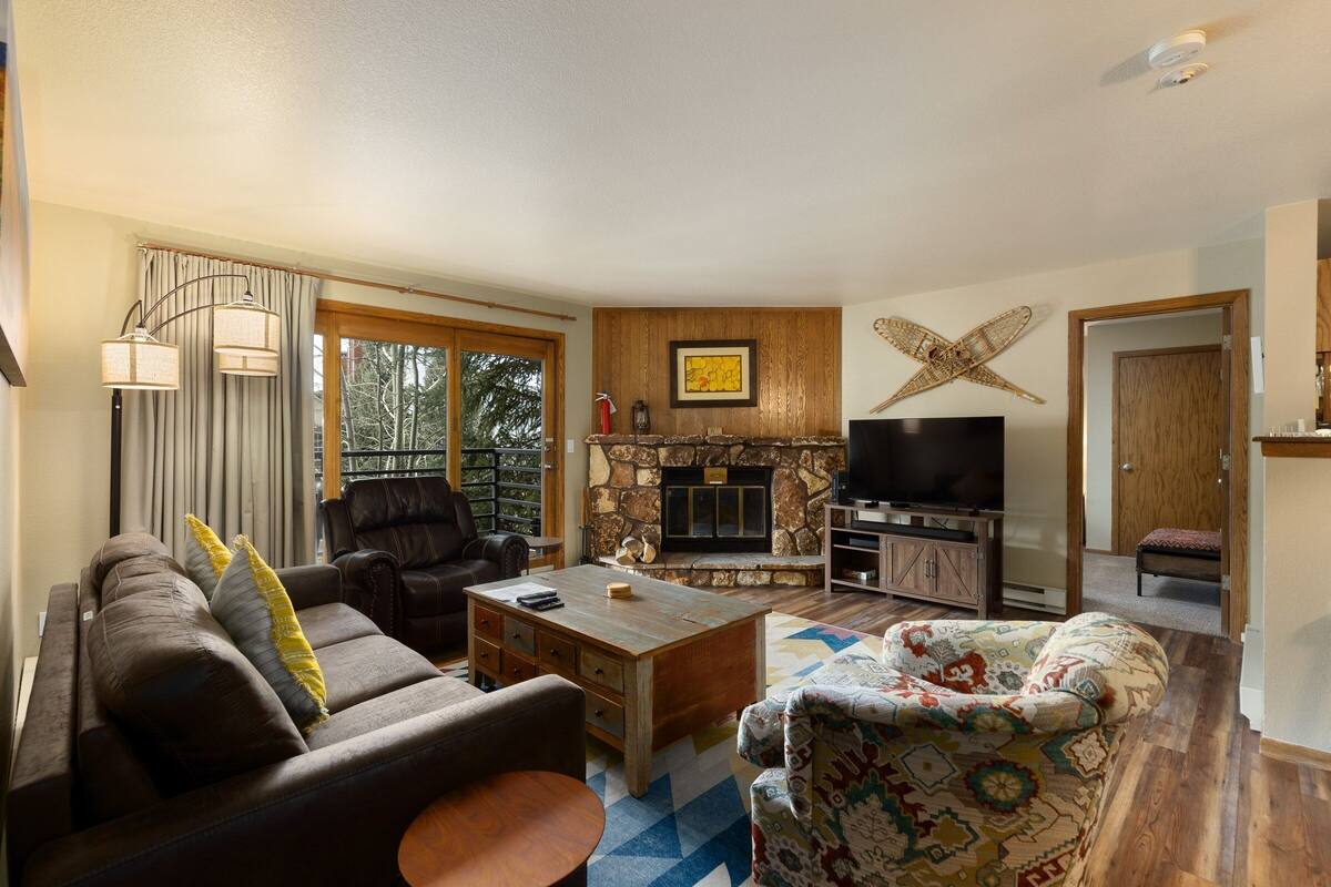 Una sala de estar con chimenea de piedra, televisión y un ventanal con cortinas.