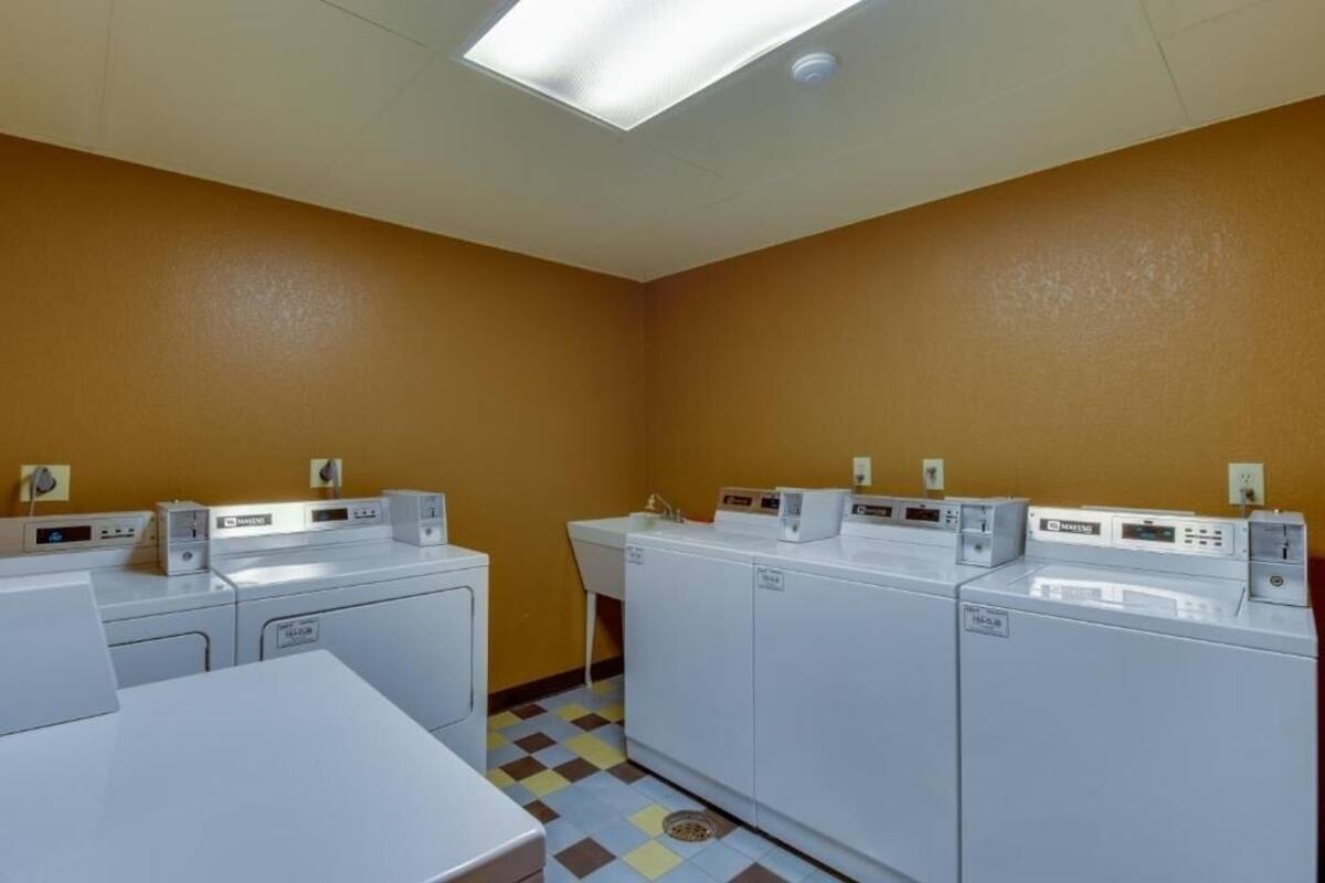 Una sala de lavandería con cuatro lavadoras blancas, un lavabo y piso de baldosas.