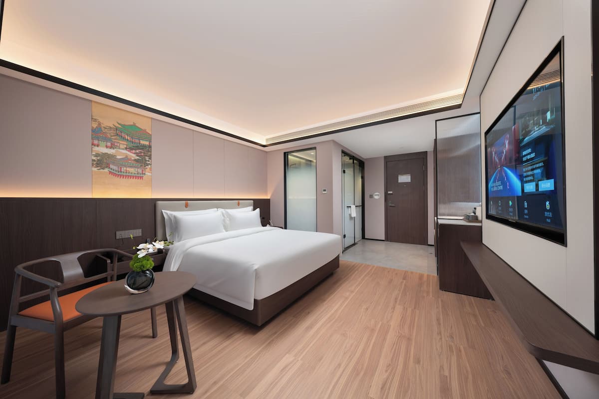 Una habitación de hotel moderna con una cama grande, un escritorio, una silla, un televisor y un cuadro en la pared.