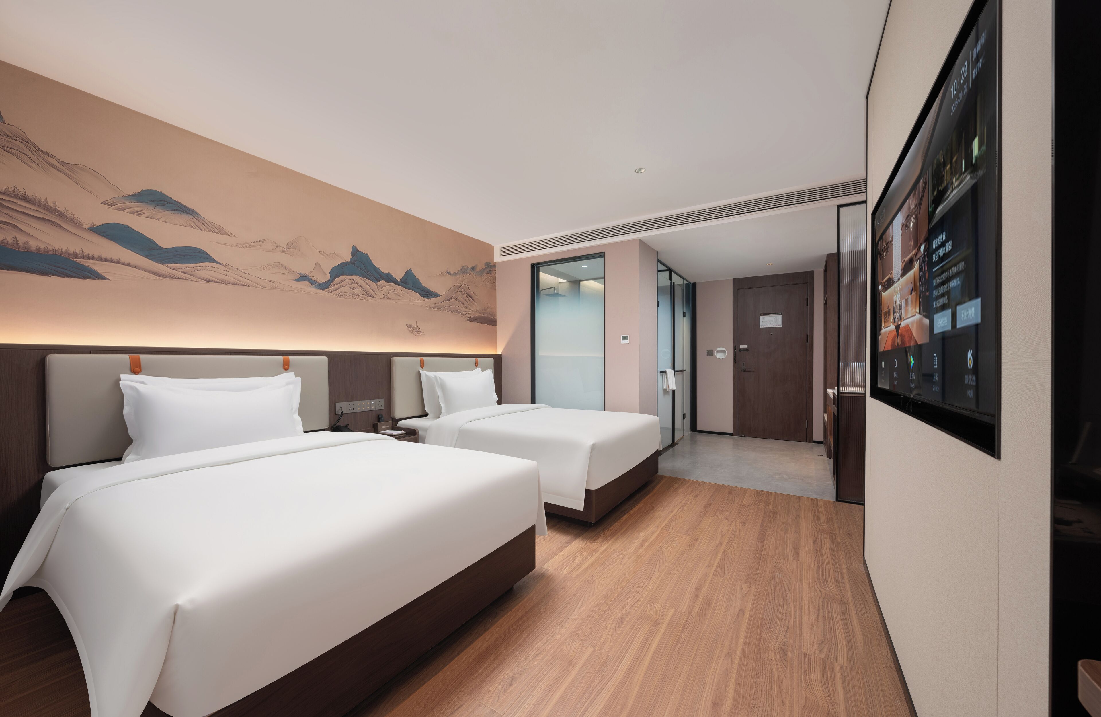 A hotel room with two beds, a large wall mural, and a digital display on the wall.