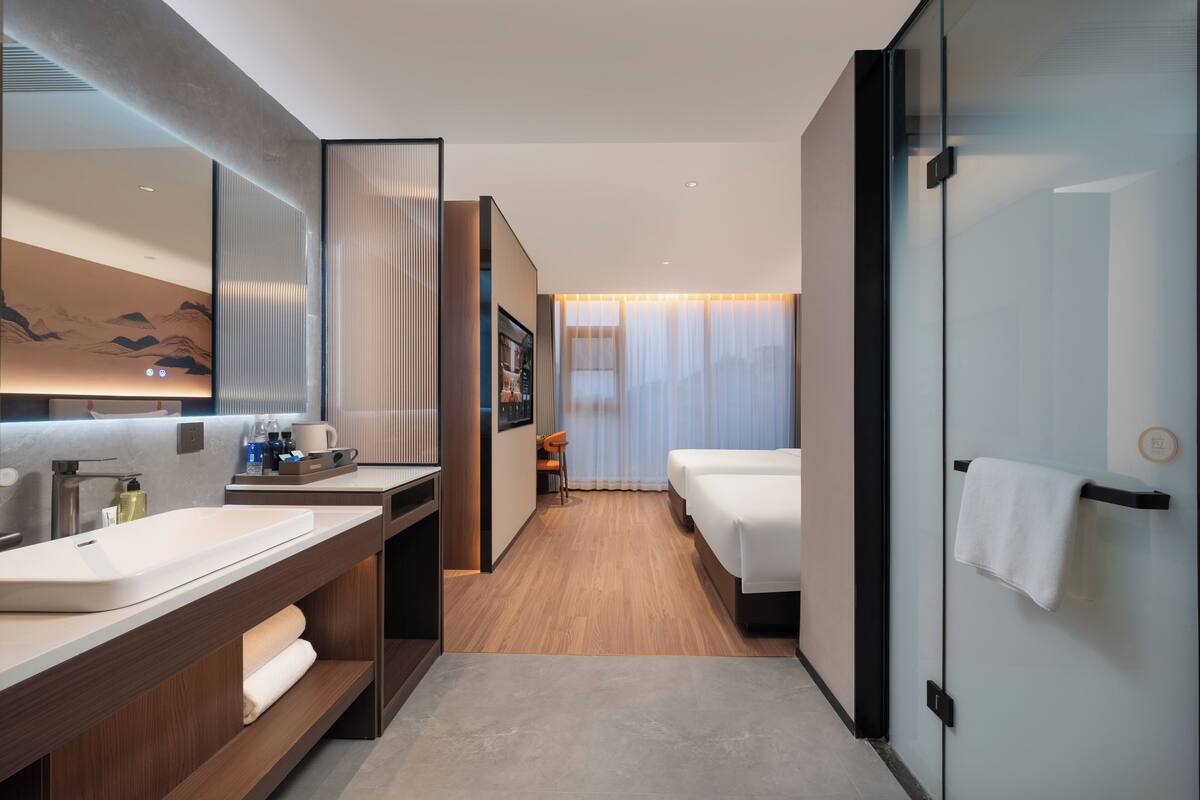 Una habitación de hotel moderna con un espejo grande, un tocador de madera, una cama y una puerta de vidrio.