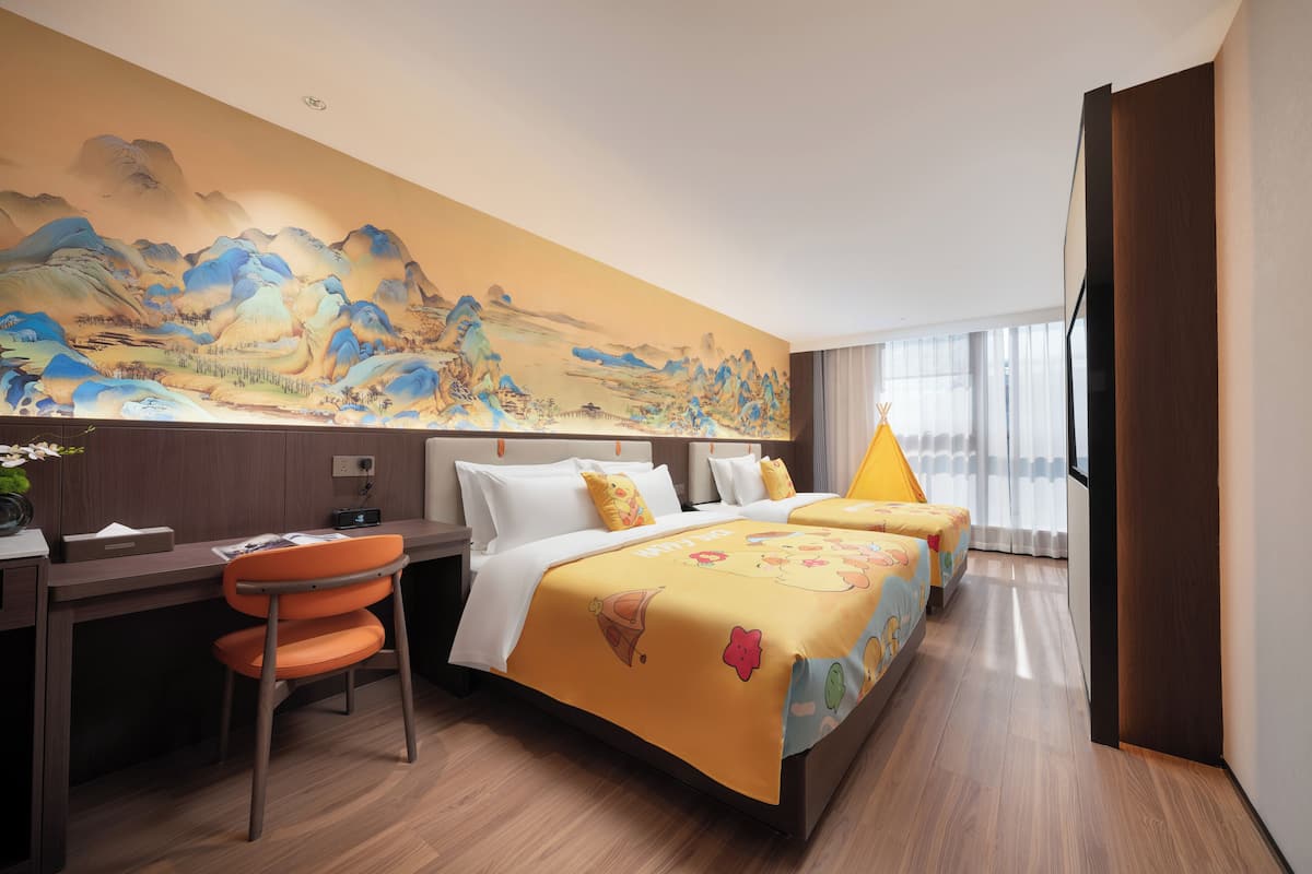 Una habitación de hotel con cama, escritorio y silla, un mural grande en la pared y una ventana con cortinas.