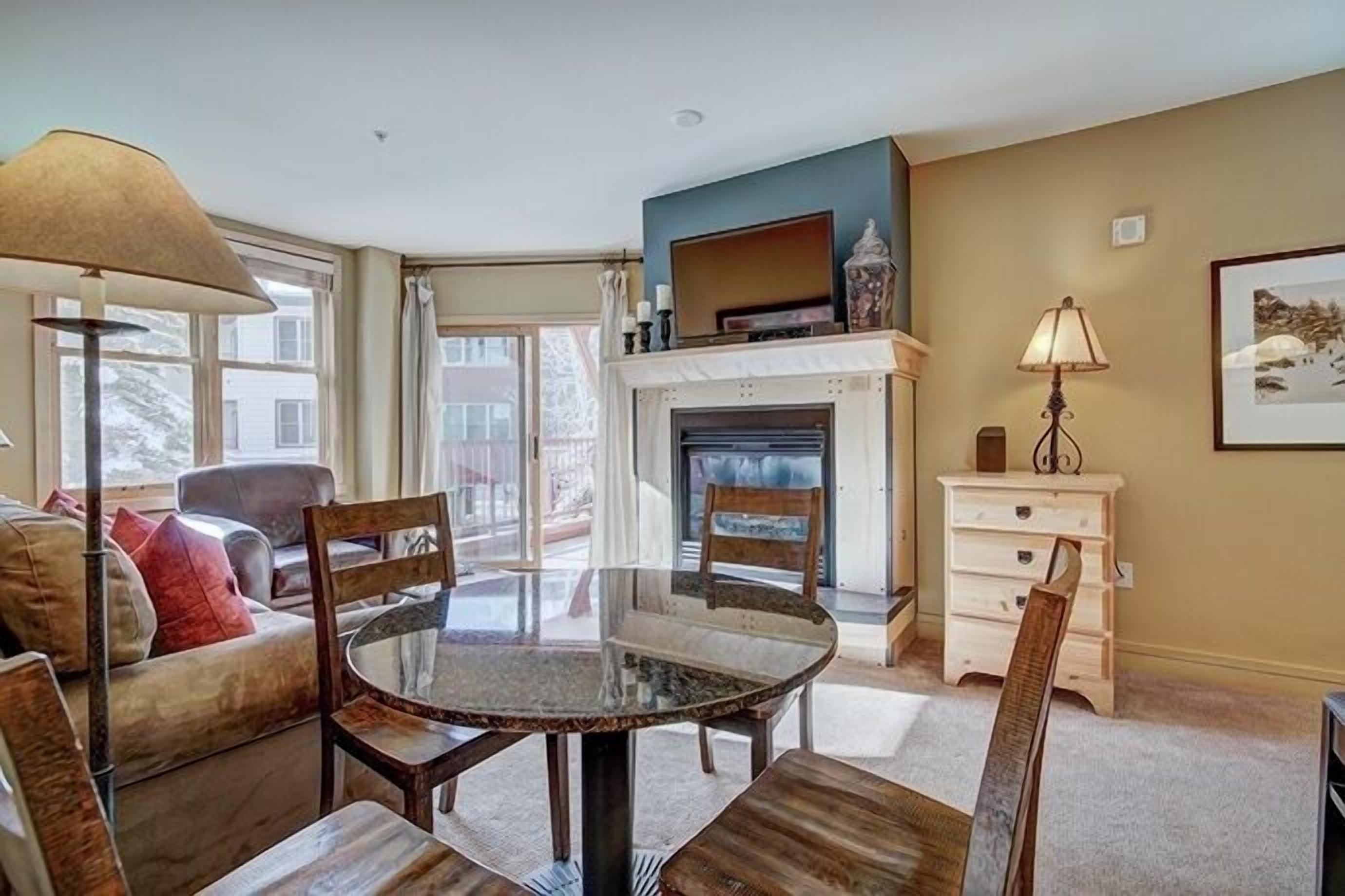 A living room with a glass-top table, wooden chairs, a sofa, a fireplace, and a television on a stand.
