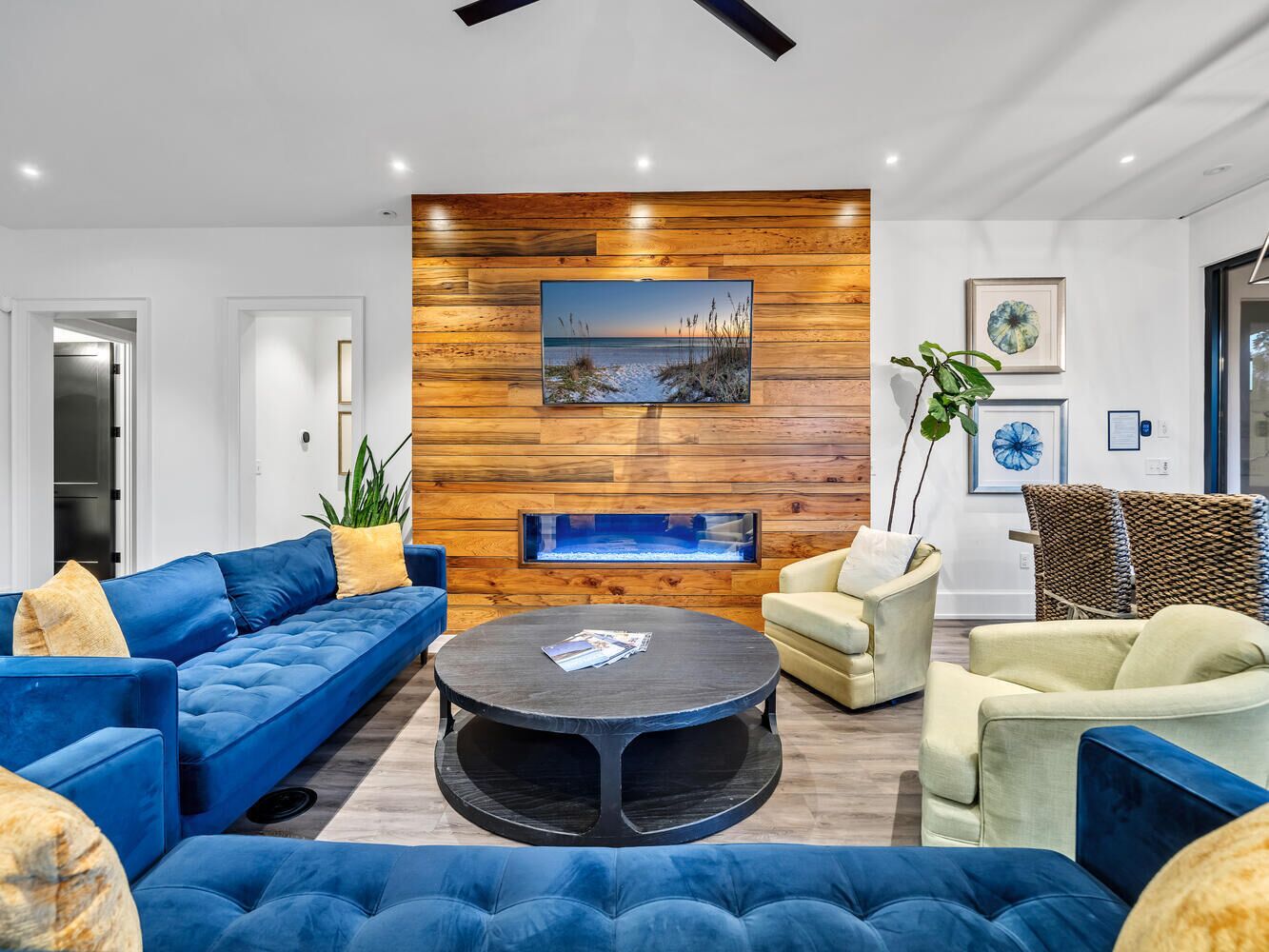 Een moderne woonkamer met een blauwe zithoek, een ronde salontafel en een houten accentmuur met een schilderij.