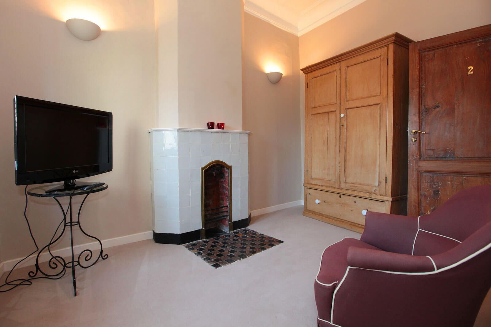 A living room with a flat-screen TV, a fireplace, a large wooden wardrobe, and a red armchair.