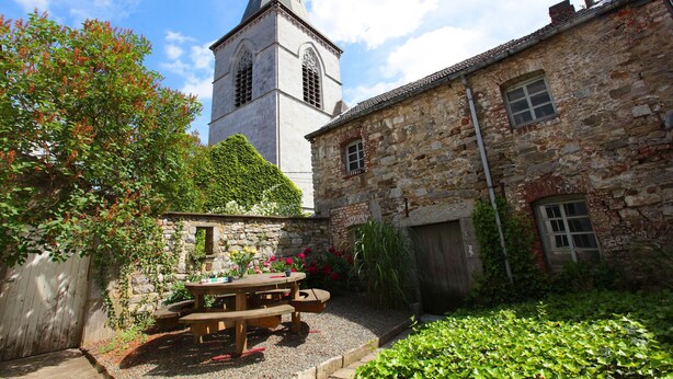 A courtyard with a stone building, a wooden table, and a tower in the background. - Spacious, Luxurious, & Cozy Holiday Home - Le Dragon Limbourg (Limbourg)