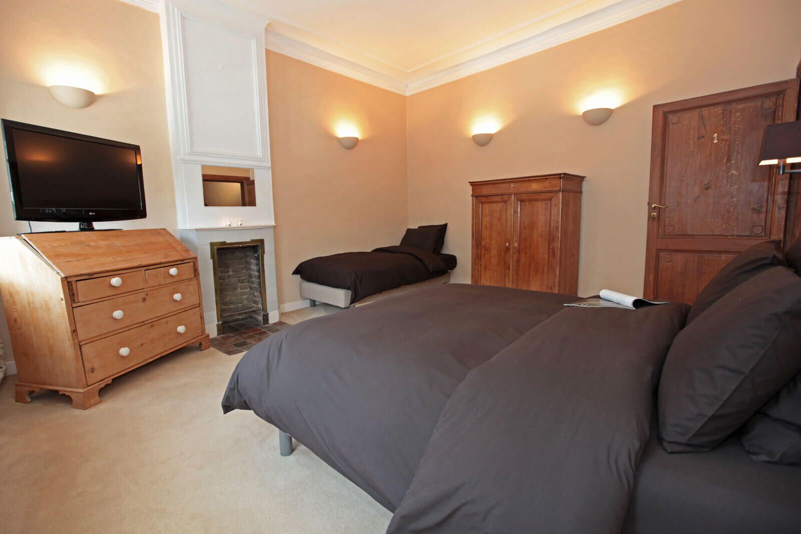 A bedroom with a large bed, a wooden dresser, a television, and a fireplace.