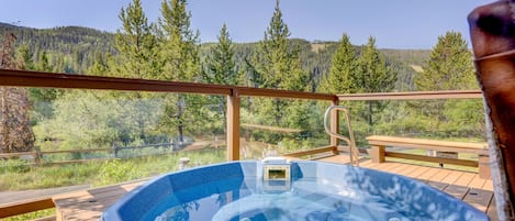 A hot tub on a wooden deck with a clear view of a forested hillside.