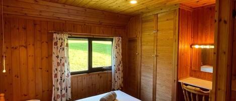 A wooden cabin room with a bed, a desk, and a window.