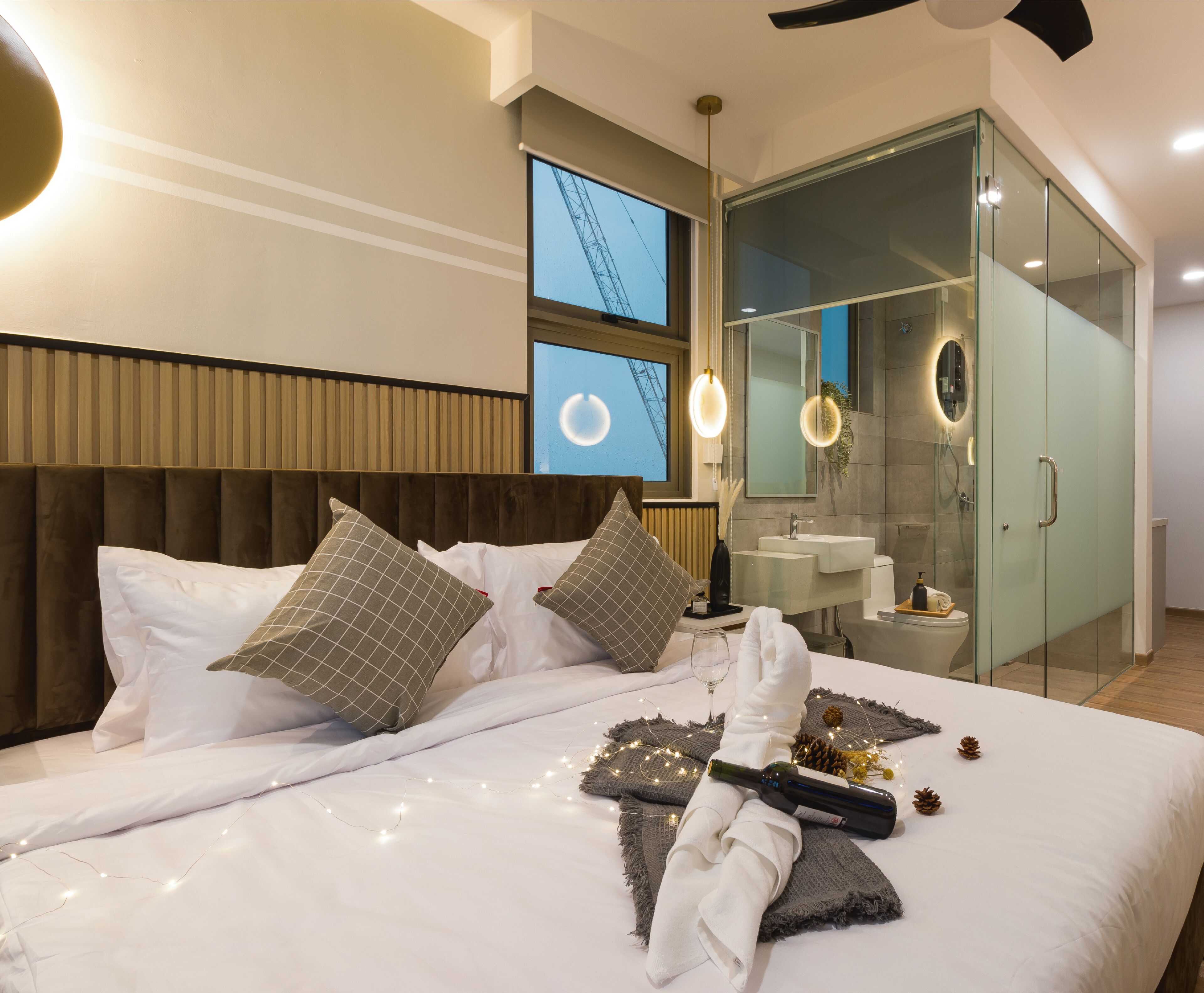 A modern hotel room with a large bed, a glass-enclosed bathroom, and a view of the sky through the window.