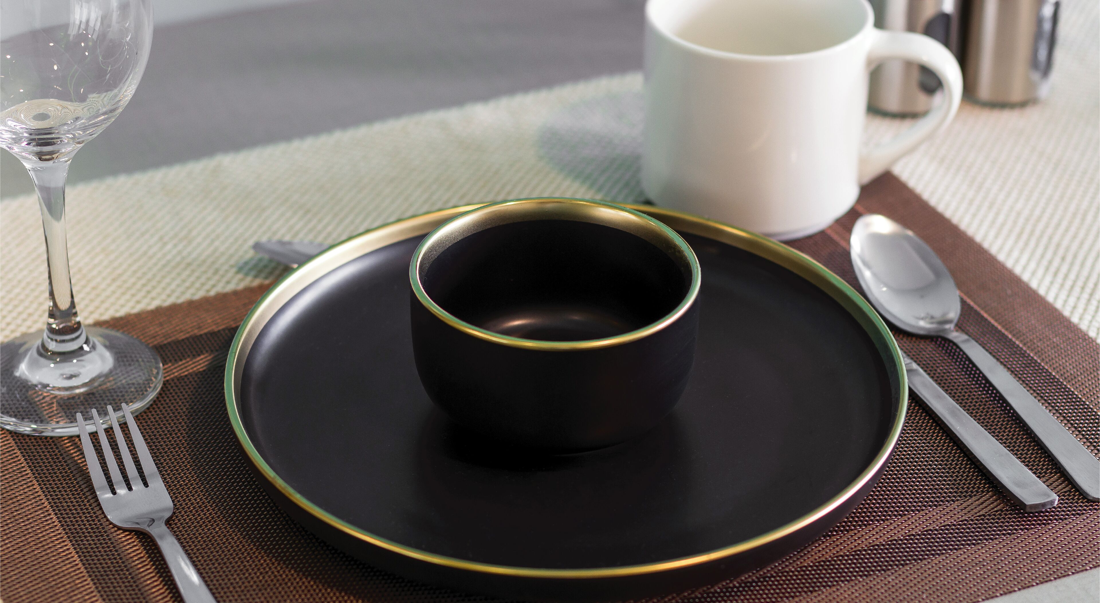 A table setting with a black plate, a cup, a fork, a spoon, and a wine glass.